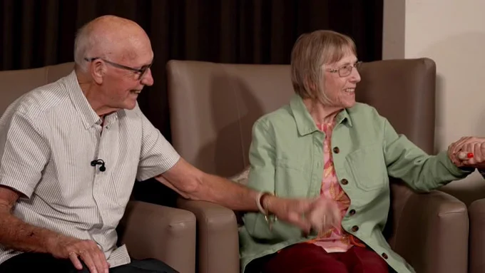 Husband and wife Ken and Mil holding hands and smiling 