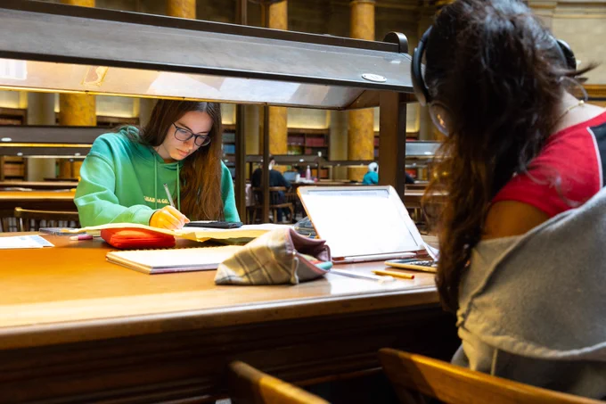 Two young women work at a table in a library.