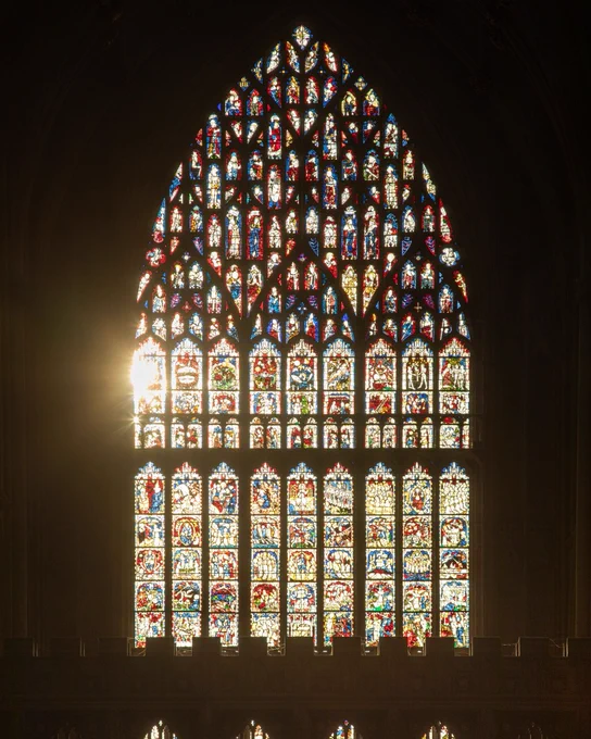 Inside York Minster cathedral. The Great East Window is illuminated by the early morning sunlight which is streaming through. The vibrant colours of this ornate window are striking agains the dark backdrop of the inside of the cathedral.