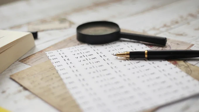 Photograph of documents spread and piled on top of each other, with a pen and a magnifying glass atop. By Andrijana Bozic under a free Unsplash license: https://bit.ly/48J7xwO.