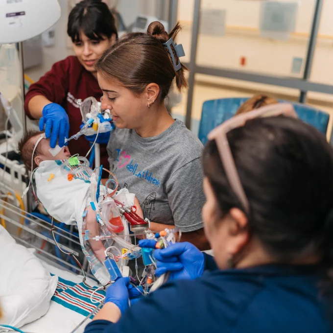 Three healthcare professionals attending to a baby in a hospital neonatal intensive care unit.