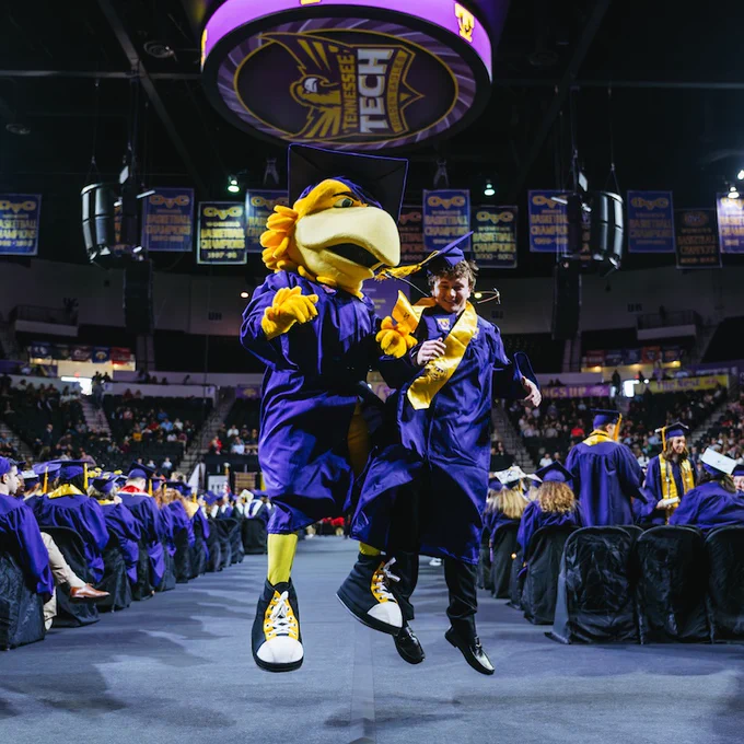 The Awesome Eagle mascot and a graduate jump in the air.