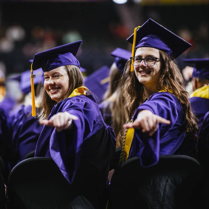 Two graduates give a wings up hand sign.