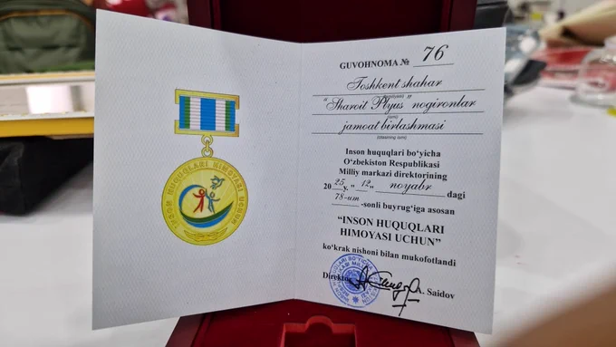Close-up of an official certificate and medal titled “For the Protection of Human Rights,” displayed in an open case.