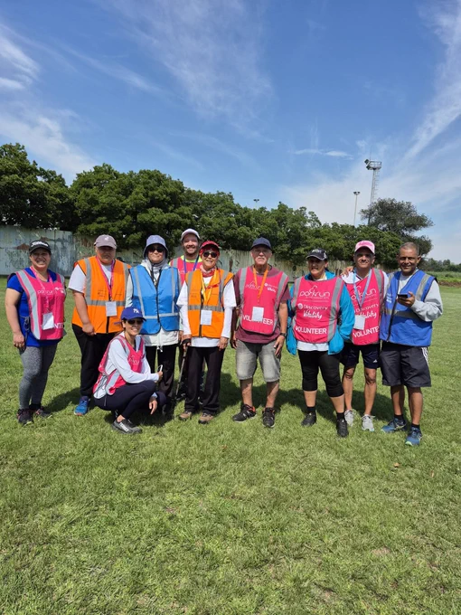 A group of parkrun volunteers taking pictures on a sunny day with green grass and trees in the background.