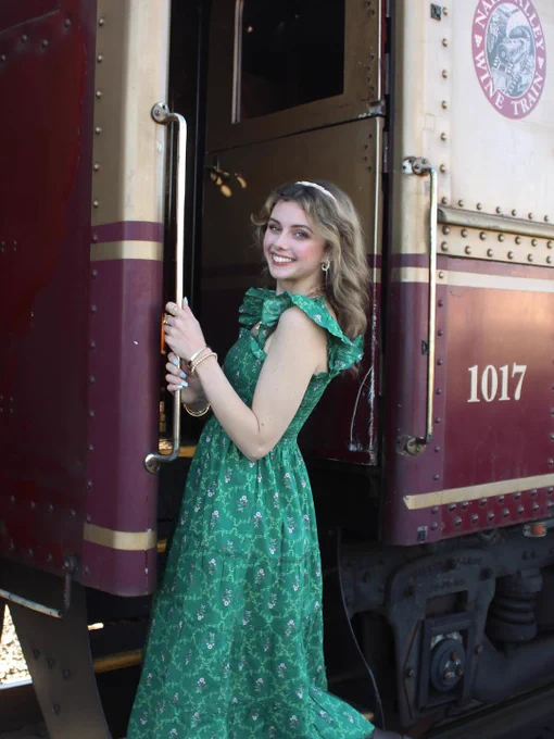 Person in a green dress smiling and standing on the steps of a Napa Valley Wine Train carriage.