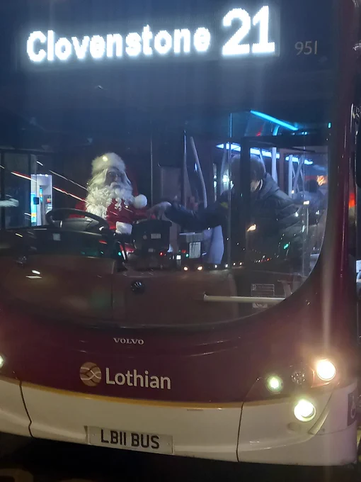 Santa Claus sitting inside a Lothian bus numbered 21 to Clovenstone at night.