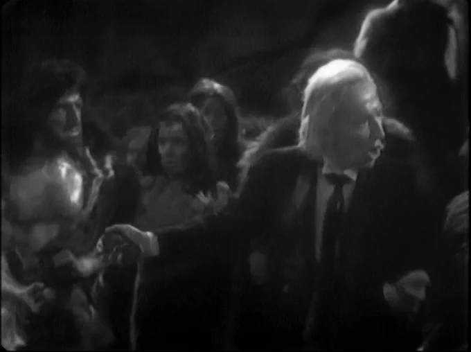 The Doctor (William Hartnell) holding court before the fur-clad Stone Age Tribe of Gum, putting Kal behind him
