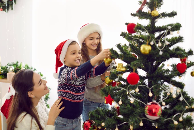Three people decorating a Christmas tree, wearing Santa hats.