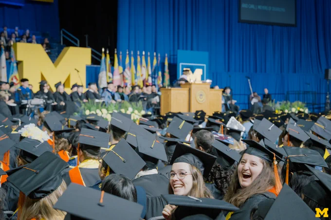 Two graduates turn around and smile during 2025 Winter Commencement at Crisler.