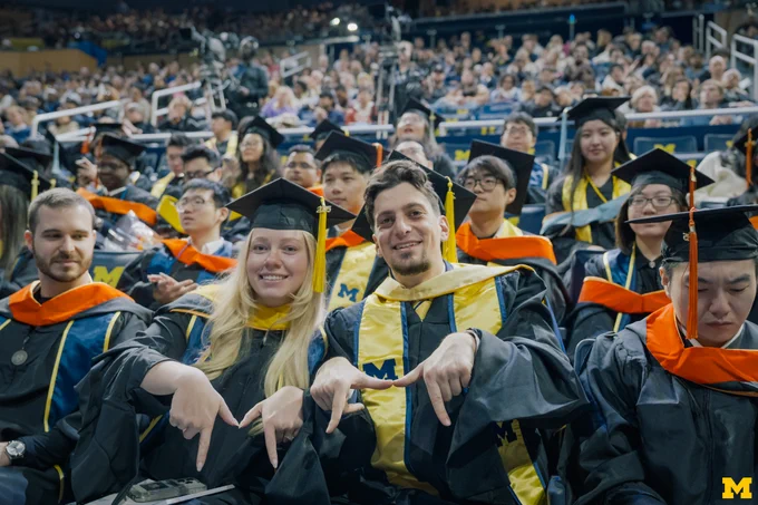 Two graduates make the Block M with their hands at 2025 Winter Commencement at Crisler Center.