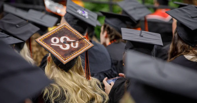 Graduation caps at a ceremony, one decorated with the logo of Oklahoma State University.