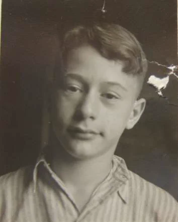 Black and white portrait photograph of a young boy with a subtle smile, wearing a striped shirt.