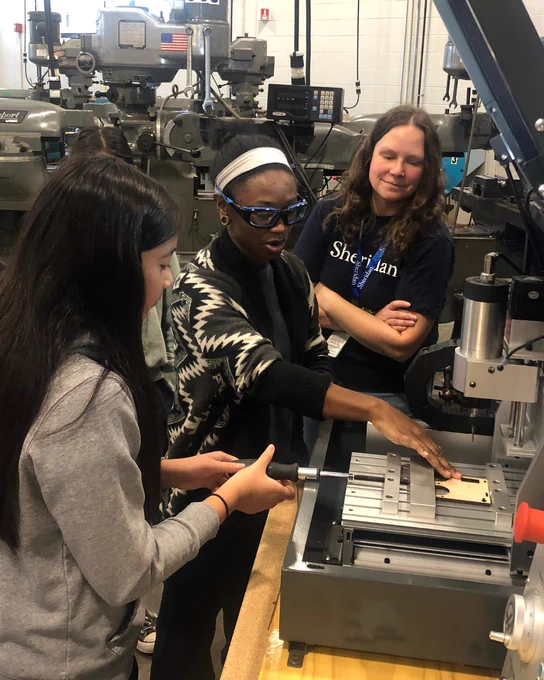 A STEM Role Model guides a youth operating equipment in a skilled trades workshop.