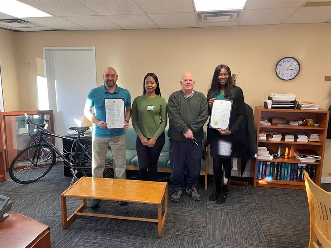 A group of four people stand together while two hold something that looks like an award of proclamation for Injury Prevention Day. 