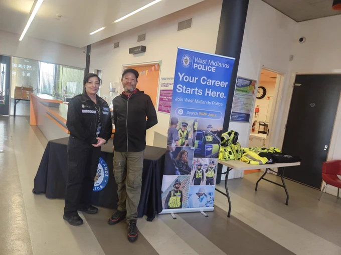 PC Begum and BABA standing by the table set up with the banner