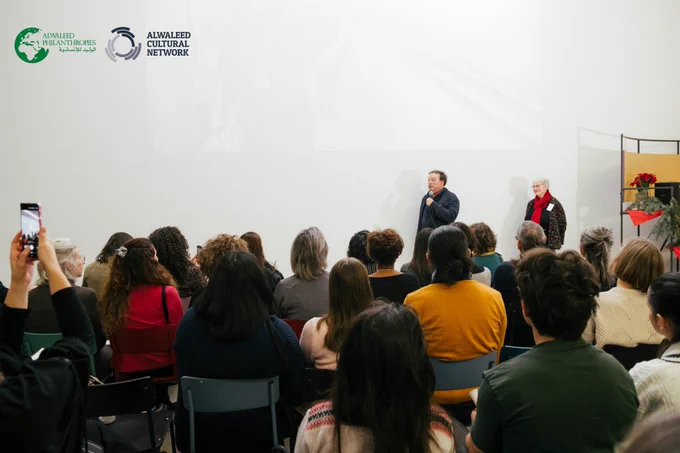 Professor Dr Stefan Weber and Dr Silke Ackermann speaking in front of an audience of people at the Multaka Anniversary Event. Professor Dr Weber is speaking into a microphone. Dr Ackermann is wearing a magenta scarf.