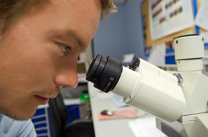 a curious college student looks through a microscope in a biology lab