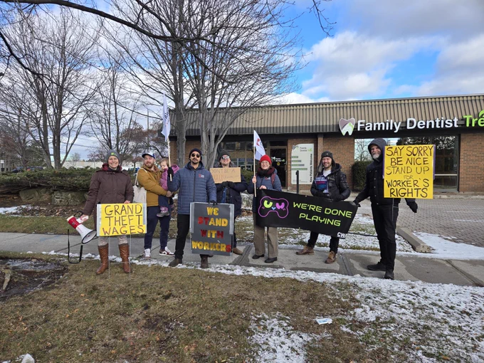 Union members outside Rockstar Toronto's studio with banners that say "Grand Theft Wages" and "We're Done Playing"