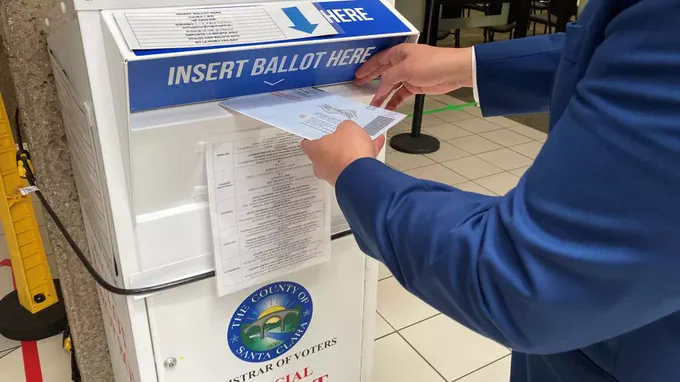 a person sticking a ballot into a ballot box. 