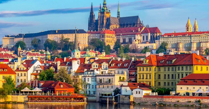 Panoramic view of Prague featuring the Prague Castle and Charles Bridge, with historical buildings along the Vltava River under a clear sky.