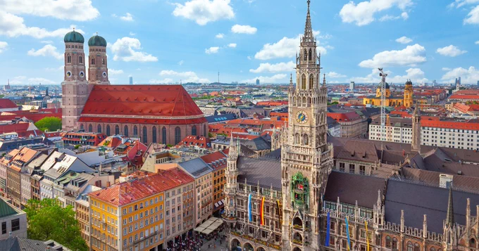 A panoramic view of Munich, featuring the iconic Frauenkirche and the New Town Hall under a clear blue sky.