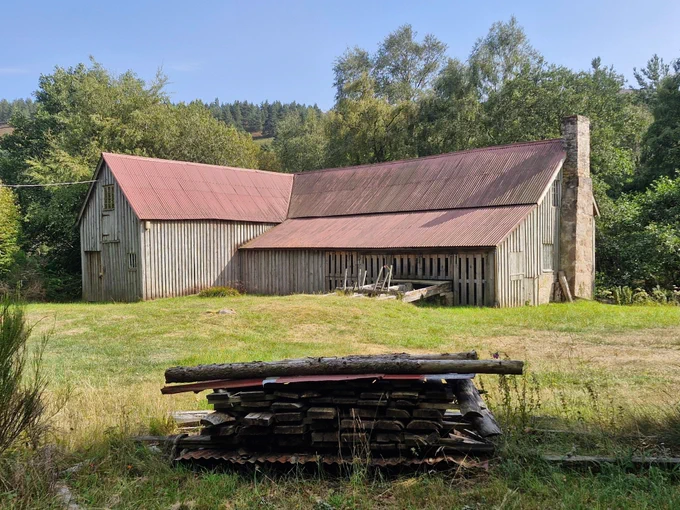 Finzean Bucket Mill, a wooden building with a metal corrugated roof. There is a pile of timbre in the foreground.