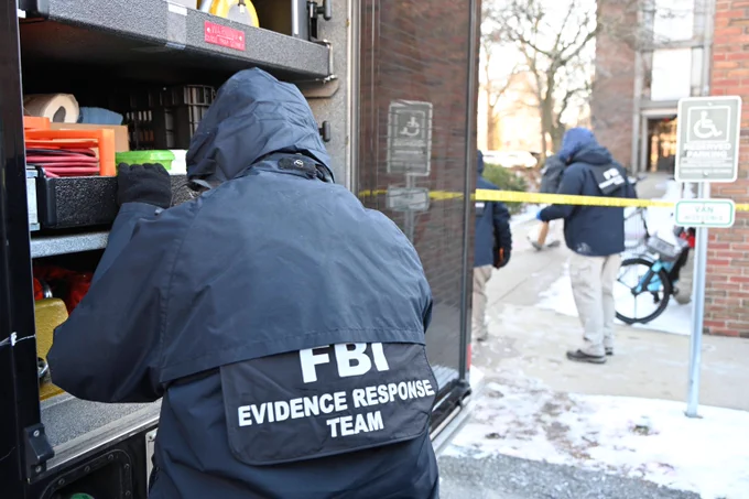FBI Evidence Response Team member in dark jacket organizing supplies inside a vehicle at a secured outdoor scene with caution tape.