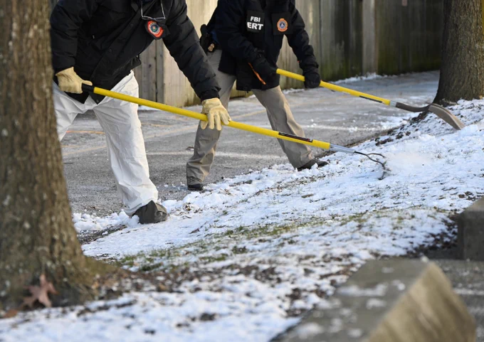 Two FBI agents using yellow tools to carefully search a snowy ground near a tree and a wooden fence.