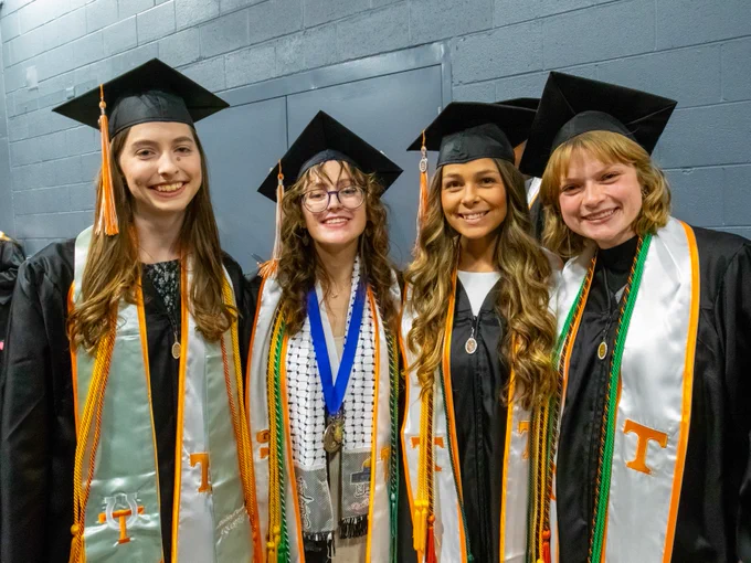 Four graduates smiling, dressed in caps and gowns with University of Tennessee insignias and various honor cords.