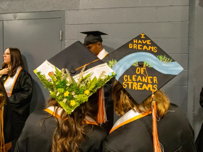 Graduates wearing decorated caps, one with 'I have dreams of cleaner streams' written on it, at a commencement ceremony.