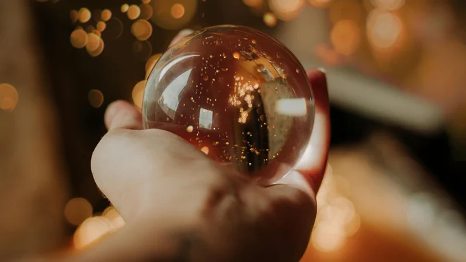 A person holding a transparent crystal ball with reflections and sparkling lights in the background. Image Credit:
Juliana Stein