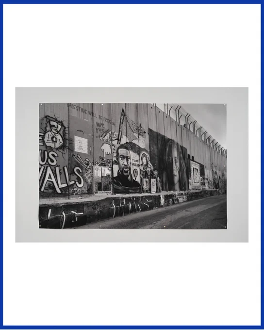 The post is framed by a dark blue border. Centred is a photo pinned to a gallery wall, depicting a section of the apartheid wall in Bethlehem, depicting murals of George Floyd, Razan al-Najjar, and Ahed Tamimi, beneath the writing "Palestine will be free" and "we refuse to die."