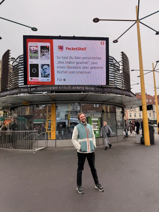 Photo of me standing before a big screen on the Graz Jakominiplatz. The screen shows a screenshot of PocketShelf next to the text:

So hast Du Dein personliches
‚Was bisher geschah". plus. einen Überblick über gelesene Bücher und Lesedauer