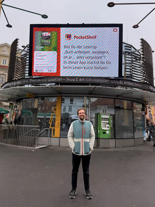 Photo of me standing before a big screen on the Graz Jakominiplatz. The screen shows a screenshot of PocketShelf next to the text:

Bist Du der Lesetyp
„Buch anfangen, weglegen, oh je ... alles vergessen"?
In dieser App machst Du Dir beim Lesen kurze Notizen.