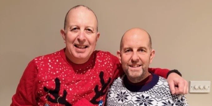 Barrie and his brother David wearing festive Christmas sweaters, one with a reindeer design and the other with a blue and white winter pattern, standing side by side indoors.