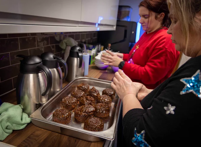 Two people preparing puddings in a kitchen with stainless steel coffee thermoses nearby.