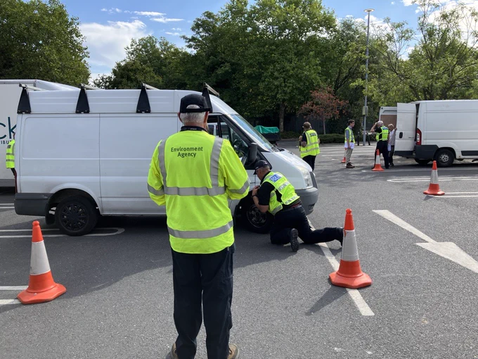 Environment Agency officer wearing high-visibility jacket inspecting a van at a road check. 