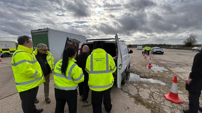 An Environment Agency officer, and other partners, in high vis jackets checking a van at a roadside stop. 