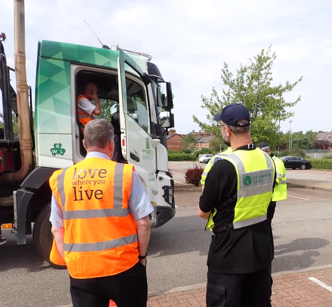 Two men, one an Environment Agency officer standing by a lorry at a road stop. 