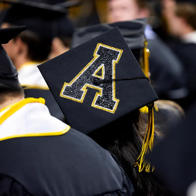 Graduate wearing a decorated cap with a glittering App State "A" at a commencement ceremony.