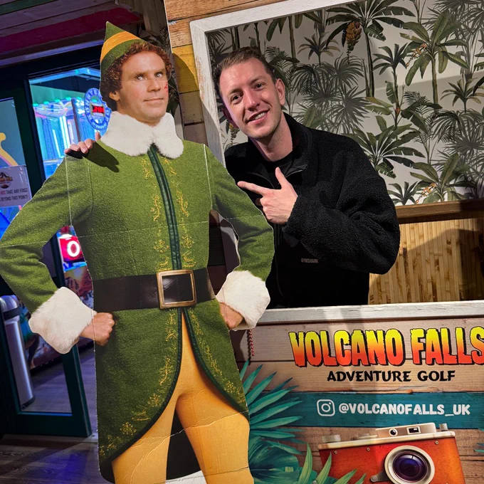 Person posing with a cardboard cutout of the character Buddy from the movie "Elf" at Volcano Falls Adventure Golf.
