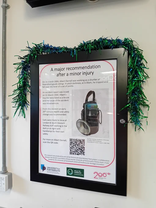 Photograph of a poster in a frame, titled 'A major recommendation after a minor injury', on a waiting room wall. A piece of green tinsel sits over the poster frame. The poster details the accident which hurt Albert Darnell.