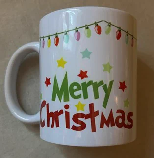 A white mug printed with the words Merry Christmas, plus Christmas lights and stars