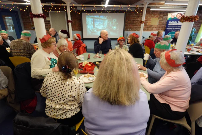 A room full of members and volunteers, sat around tables enjoying food at the Christmas party.