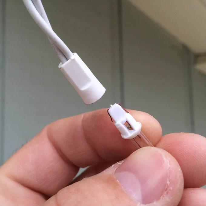 Fingers holding a mini incandescent string light bulb removed from its white plastic socket, showing the internal filament.