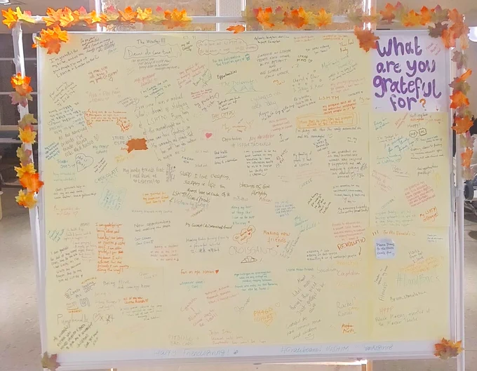 One side of the board which is surrounded by colourful autumn leaves. A sign saying "What are you grateful for?" can be seen on the right hand side of the photo.