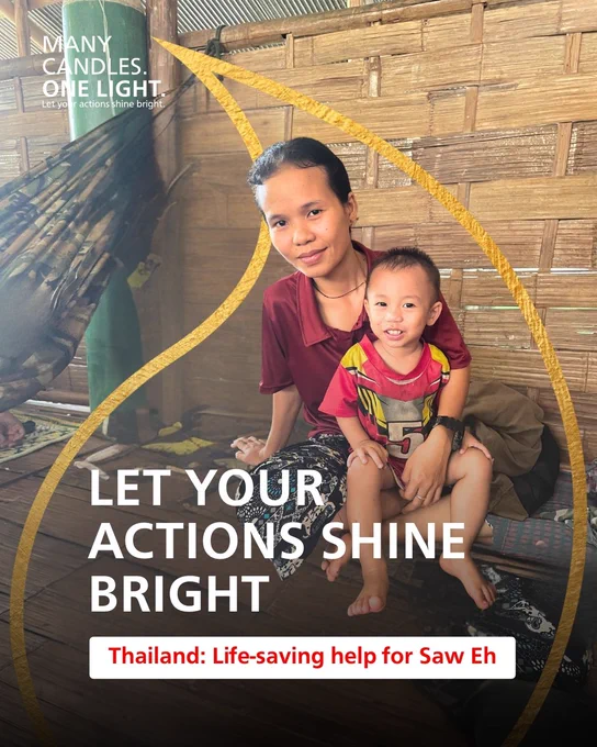 A woman and a young child sitting together in a rustic shelter with a sign promoting "Many candles. One light. Let your actions shine bright."