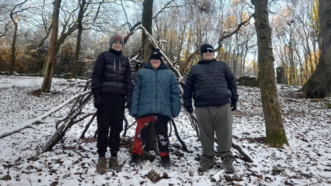 Three people standing in a snowy forest with trees behind them.