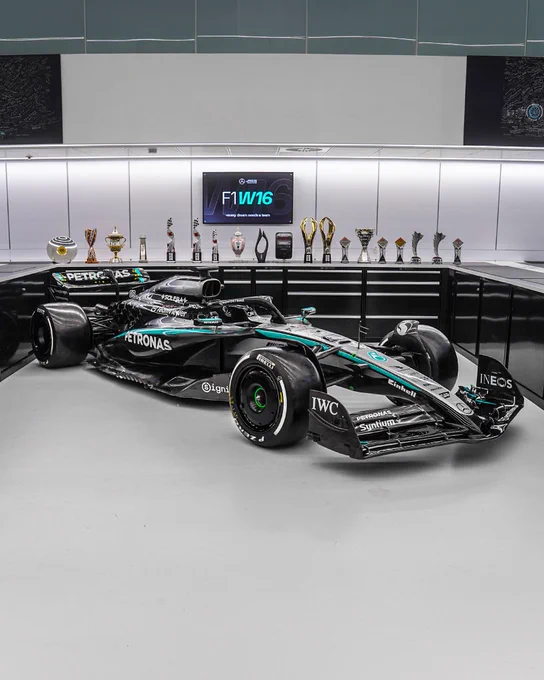 The W16 in the race bays in Brackley with the team's 2025 trophy haul placed behind in a row along the back cabinets.